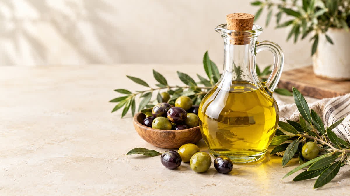 Olive oil in a glass cruet beside fresh olives and olive branches
