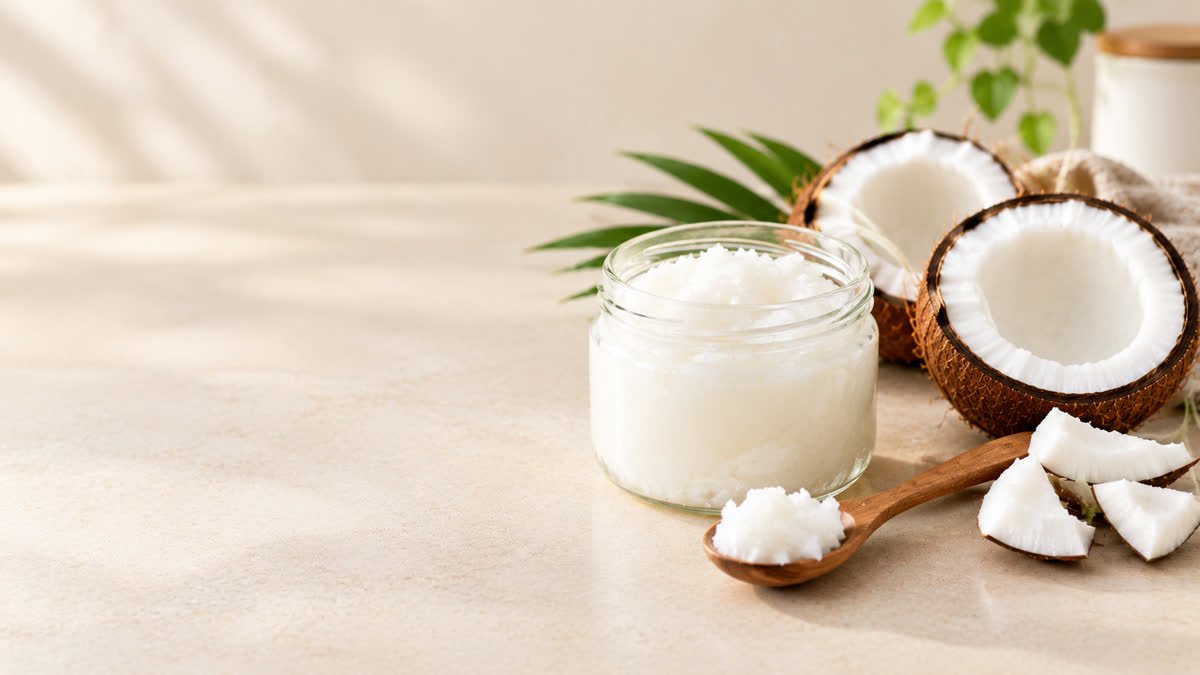 Coconut oil in a glass jar beside fresh coconut halves on a kitchen counter