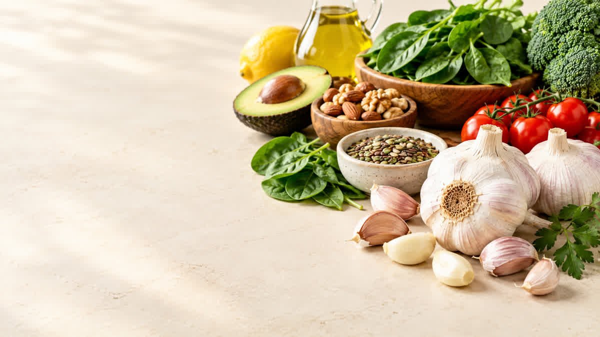 Fresh garlic bulbs and cloves beside leafy greens and lentils in a healthy food arrangement.