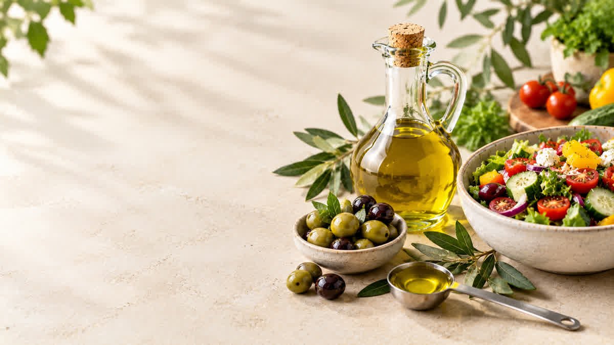 Extra virgin olive oil with fresh olives and a measuring spoon beside a vegetable salad