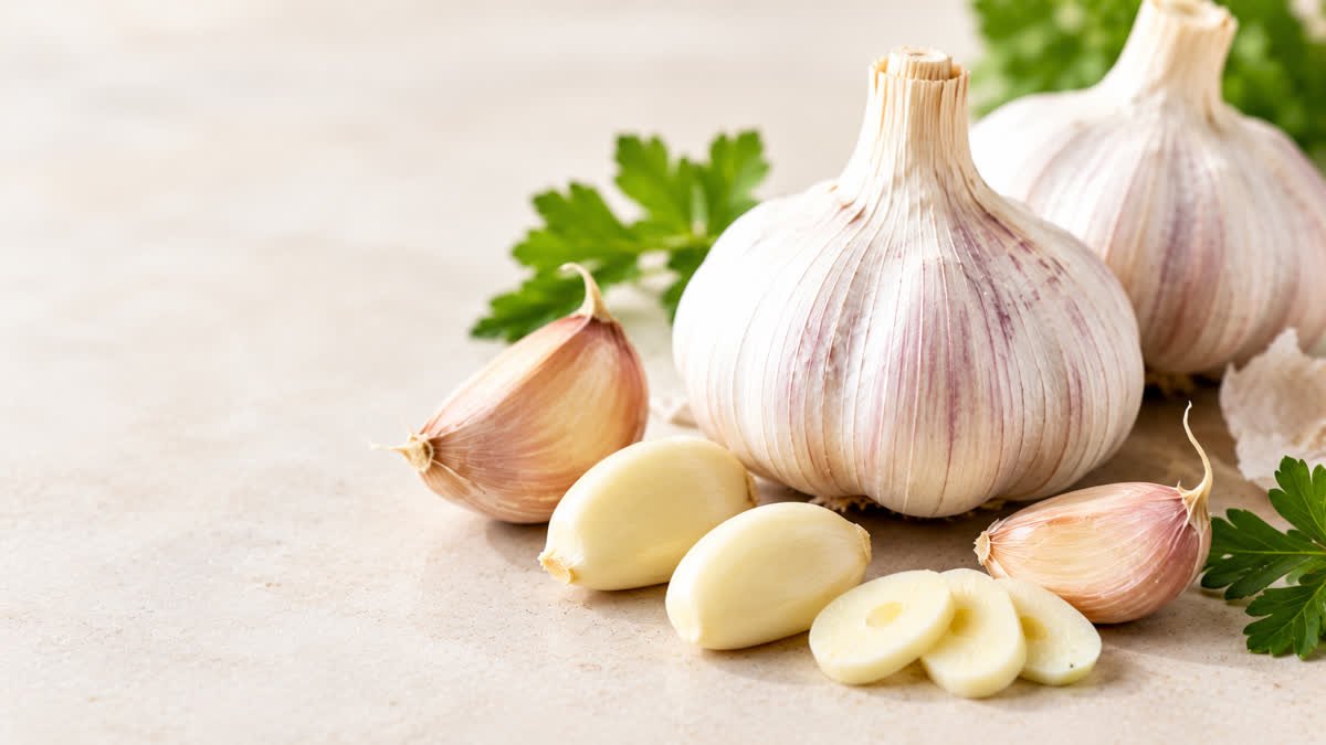 Fresh garlic bulbs and cloves alongside heart-healthy foods for an article about garlic and high cholesterol.
