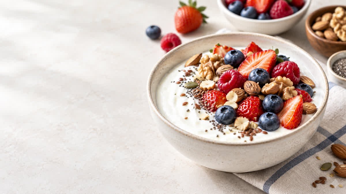 Bowl of plain Greek yogurt topped with fresh berries, walnuts, and chia seeds.