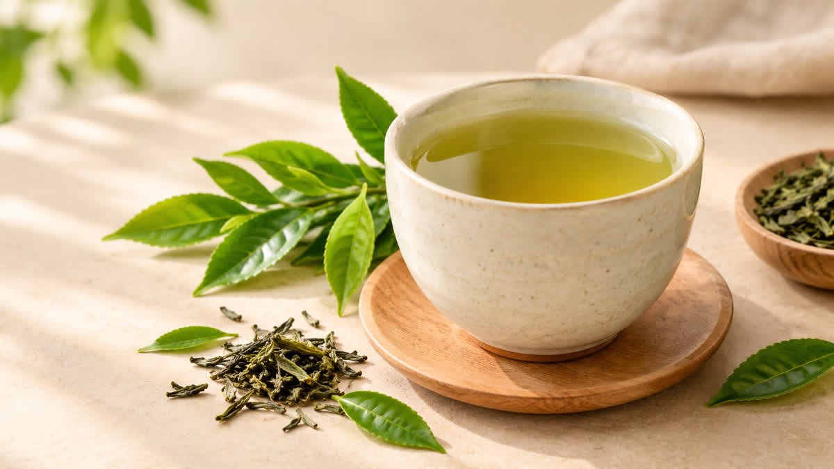 Cup of green tea with fresh tea leaves on a neutral background.
