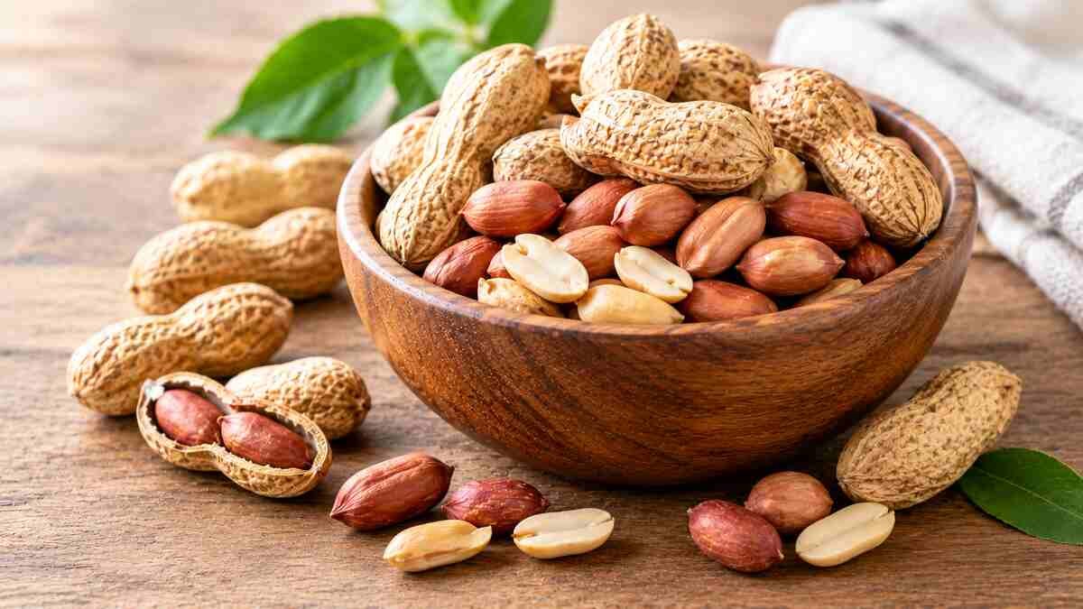 Whole peanuts in their shells and shelled peanut kernels arranged in a wooden bowl, illustrating the nutritional benefits of peanuts.