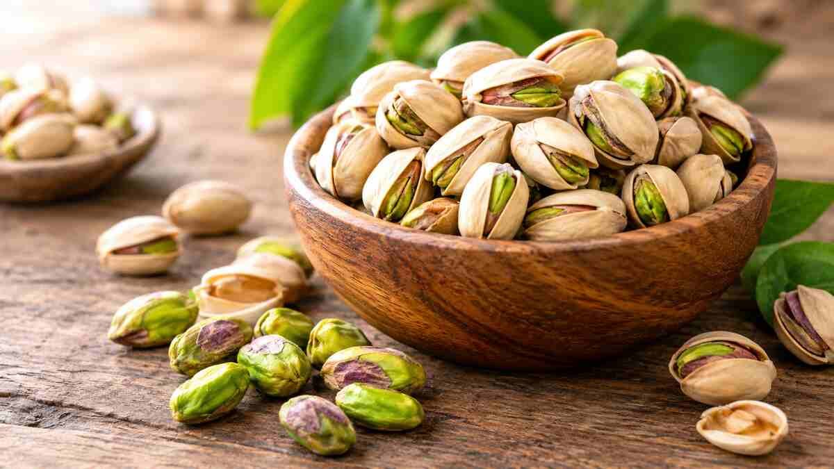 Whole pistachios in their shells and green pistachio kernels arranged in a wooden bowl, illustrating the nutritional benefits of pistachios