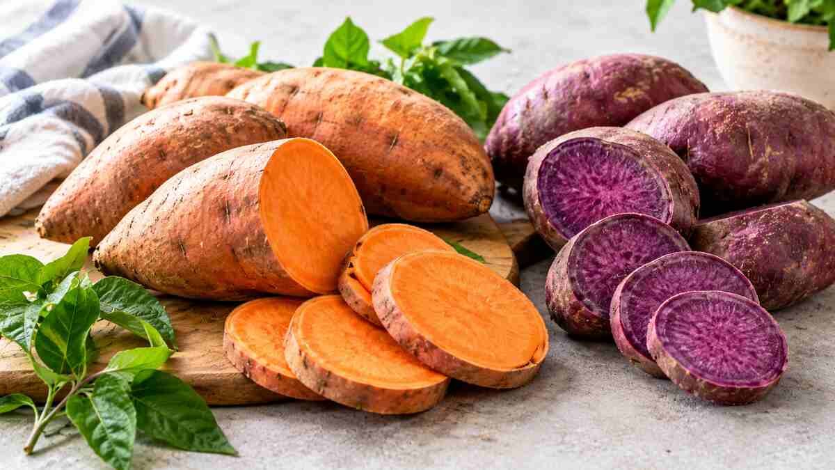 Whole and sliced orange and purple sweet potatoes arranged on a kitchen surface.