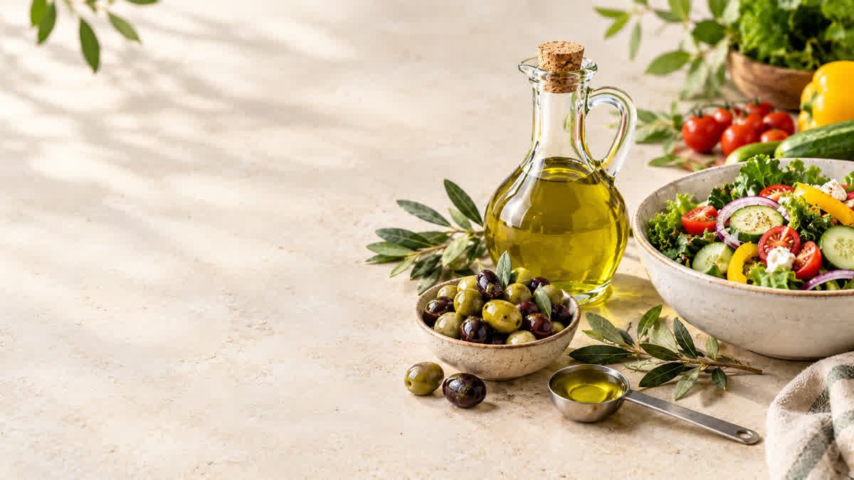 Olive oil with fresh olives and a measuring spoon beside a healthy vegetable salad